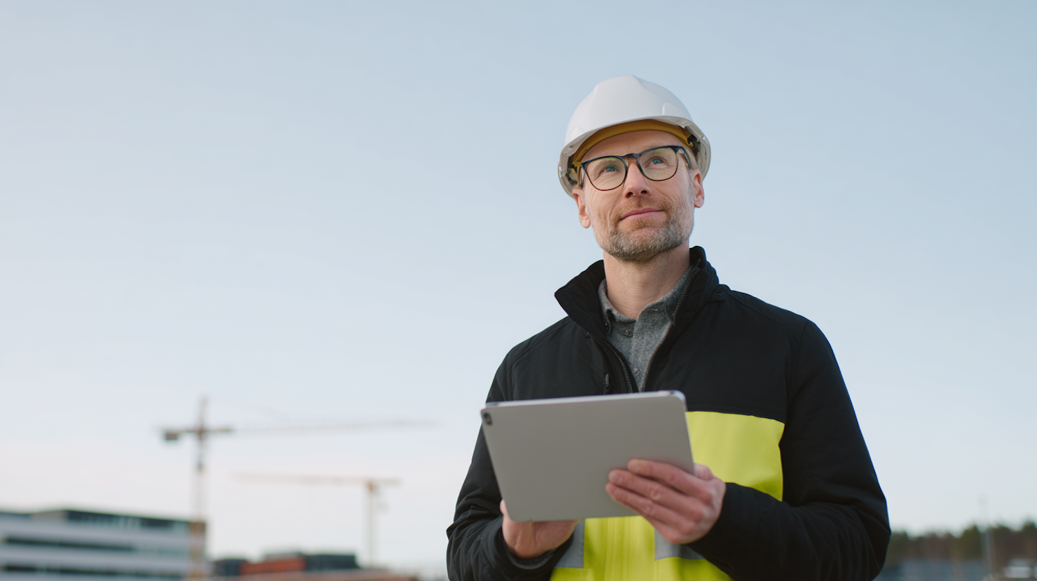 Construction professional in safety gear holding a tablet on site